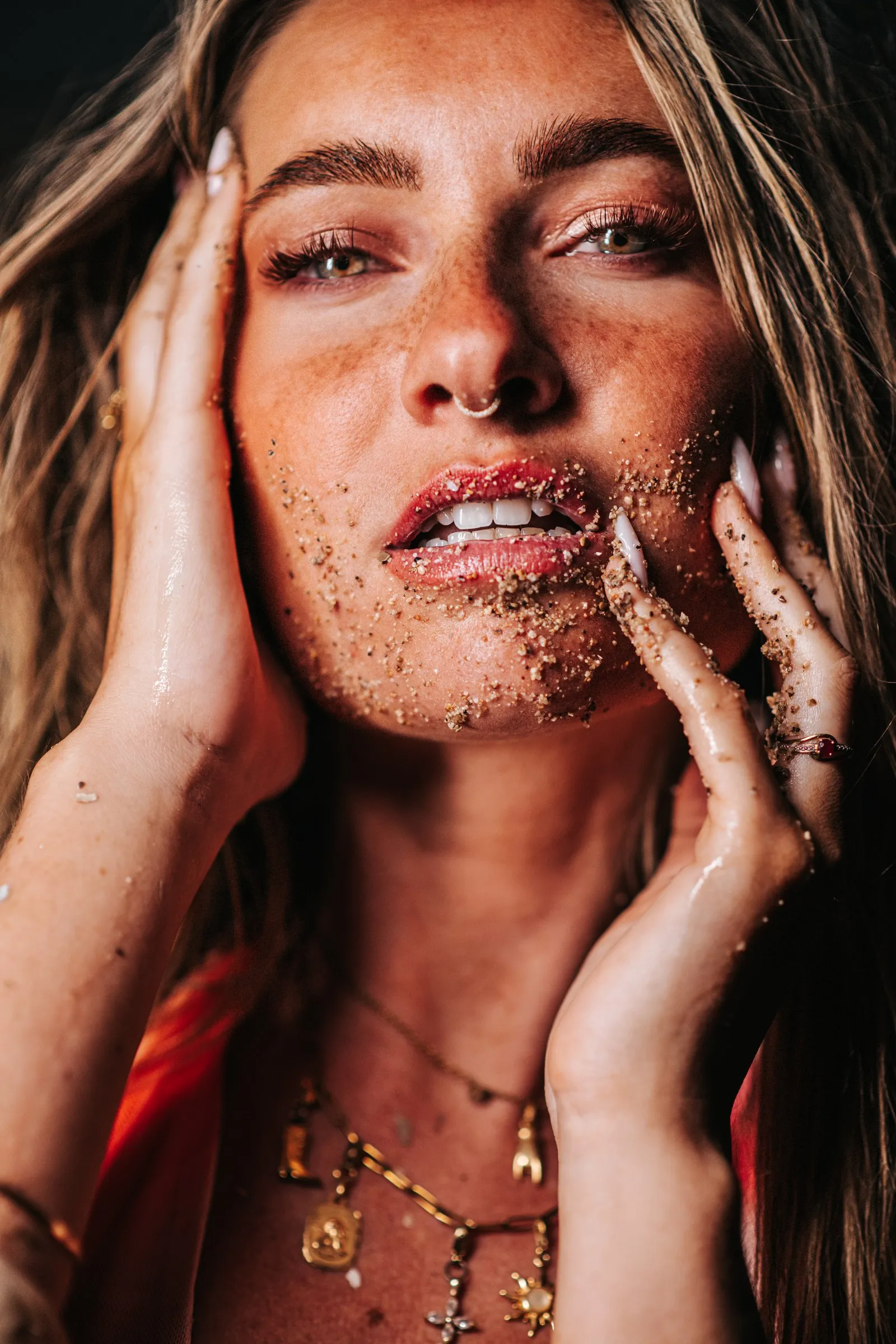 Artistic portrait: a freckled face sprinkled with grains of sand, hands framing the cheeks