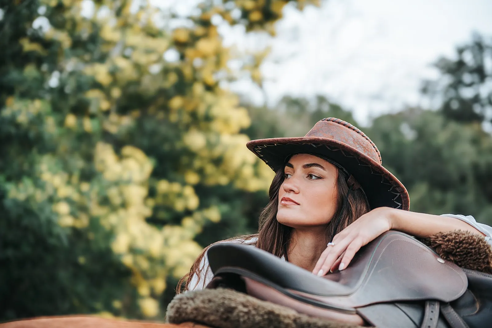 Portrait d'une jeune femme au chapeau de cuir accoudée à une selle de cheval, regard au loin, dans le Var