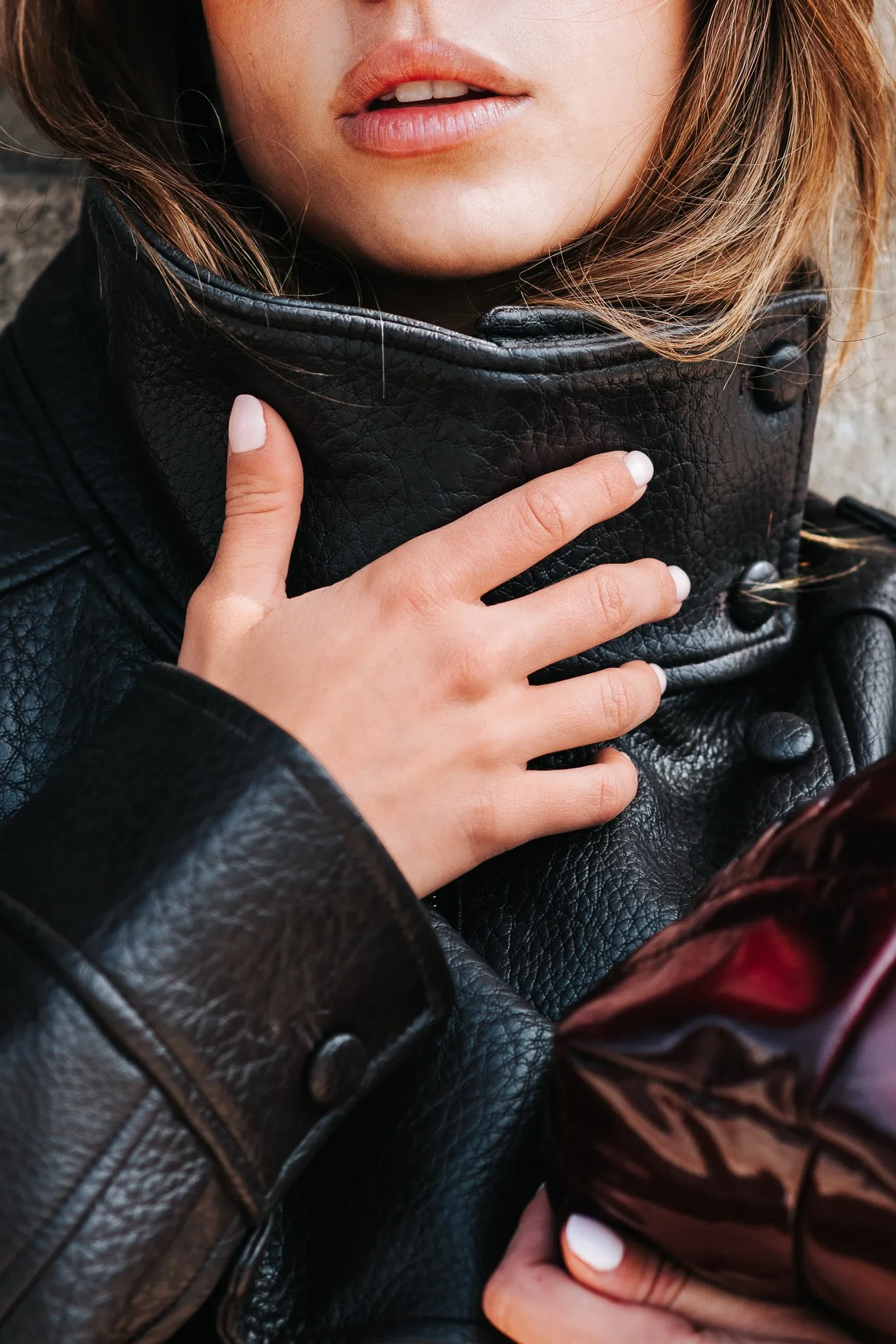 Fashion portrait detail: a hand resting on the collar of a black leather jacket, lips slightly parted