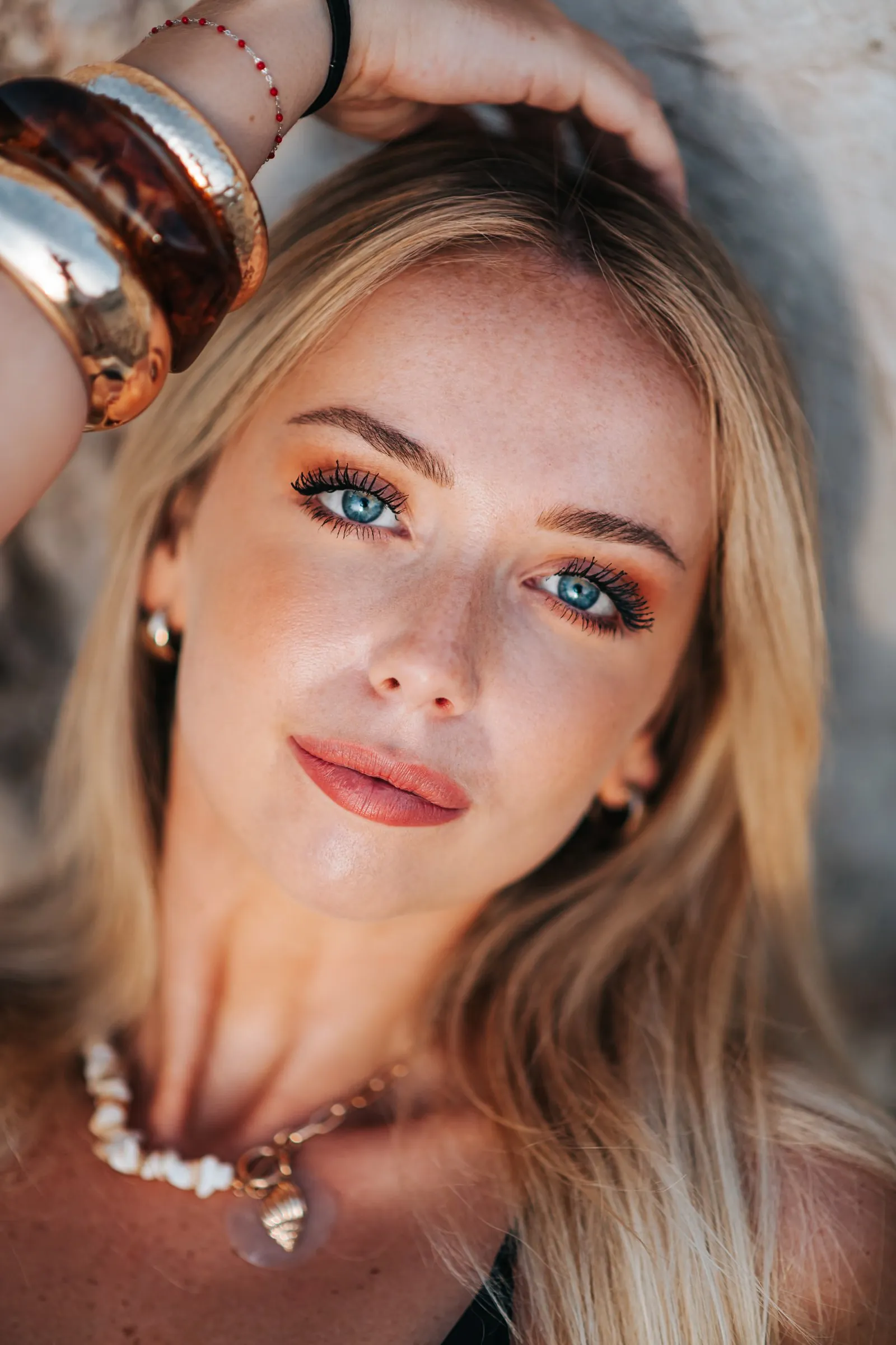 Close portrait of a blonde woman with blue eyes, hand in her hair and gold bangles on her wrist