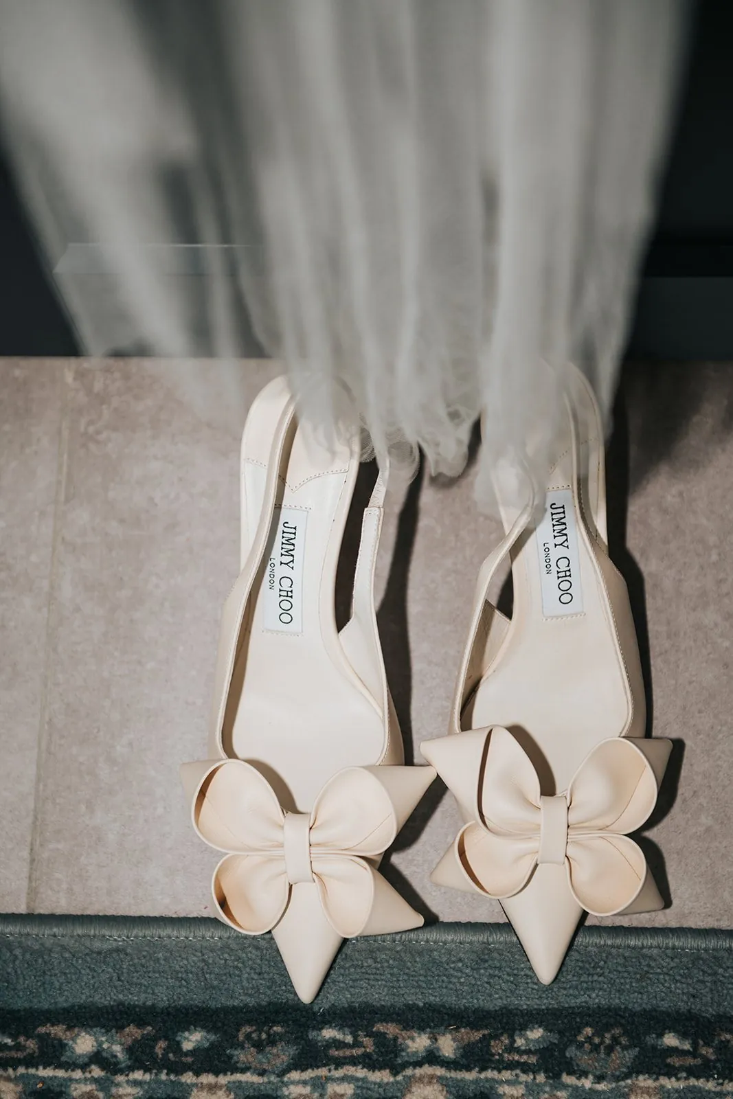 Préparatifs de mariage : escarpins crème à nœud posés au sol sous le voile de la mariée