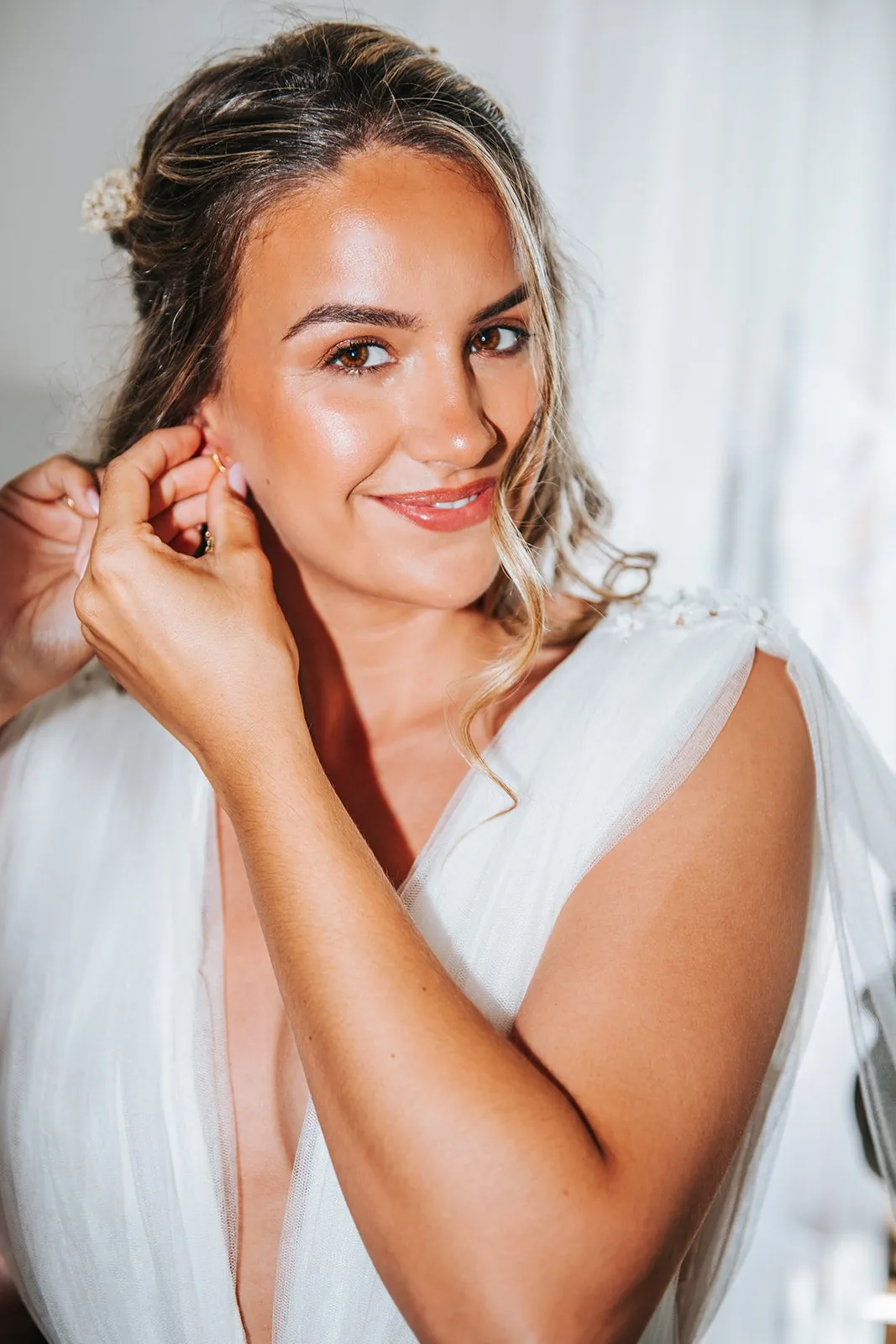 Portrait de la mariée souriante qui met ses boucles d'oreilles pendant les préparatifs, lumière douce
