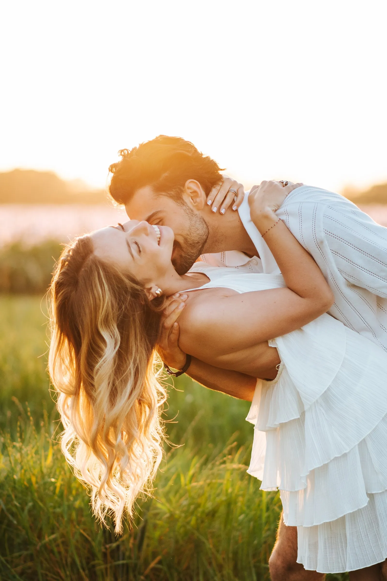 Séance couple au coucher du soleil : elle rit, renversée dans ses bras, robe blanche et cheveux dorés, à Cassis