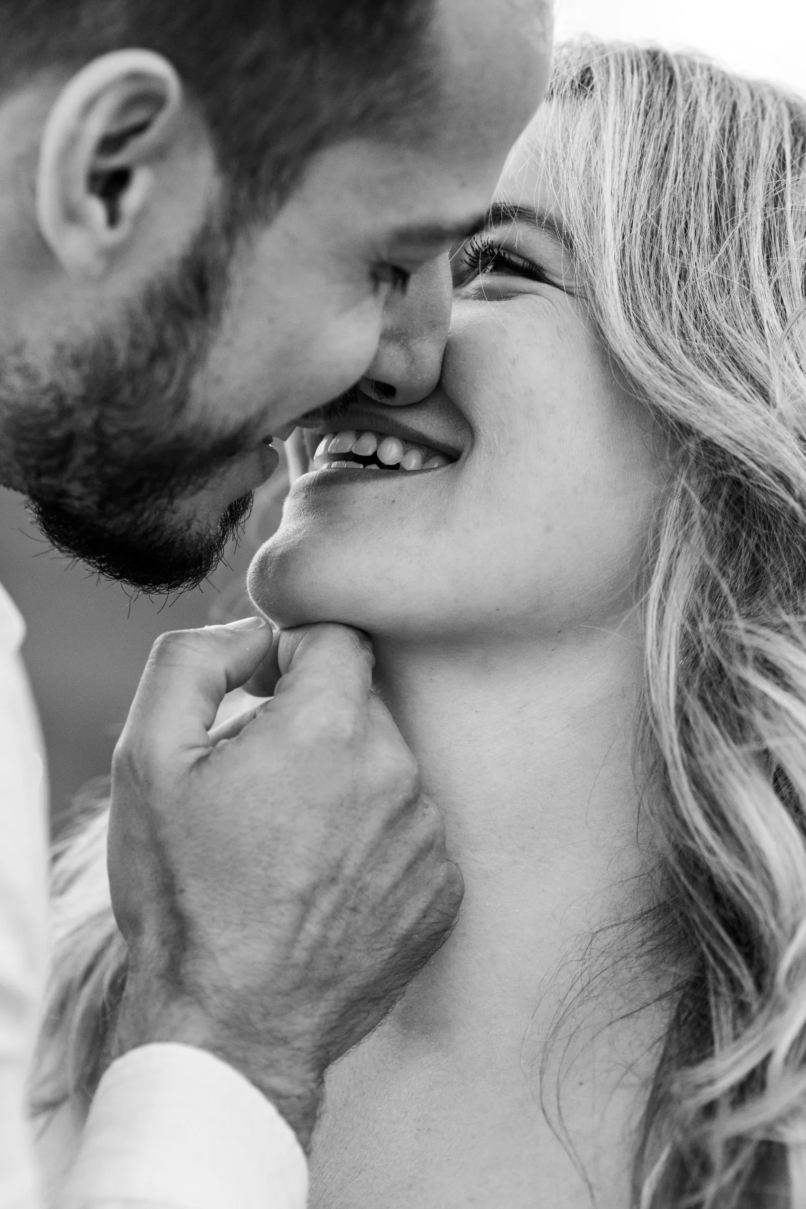 Séance couple : nez contre nez, il lui tient le menton et elle éclate de rire, portrait en noir et blanc