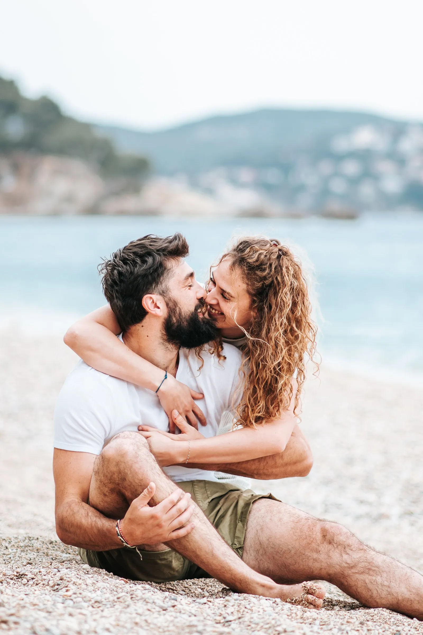 Séance couple sur la plage au coucher du soleil : ils s'enlacent face à la mer