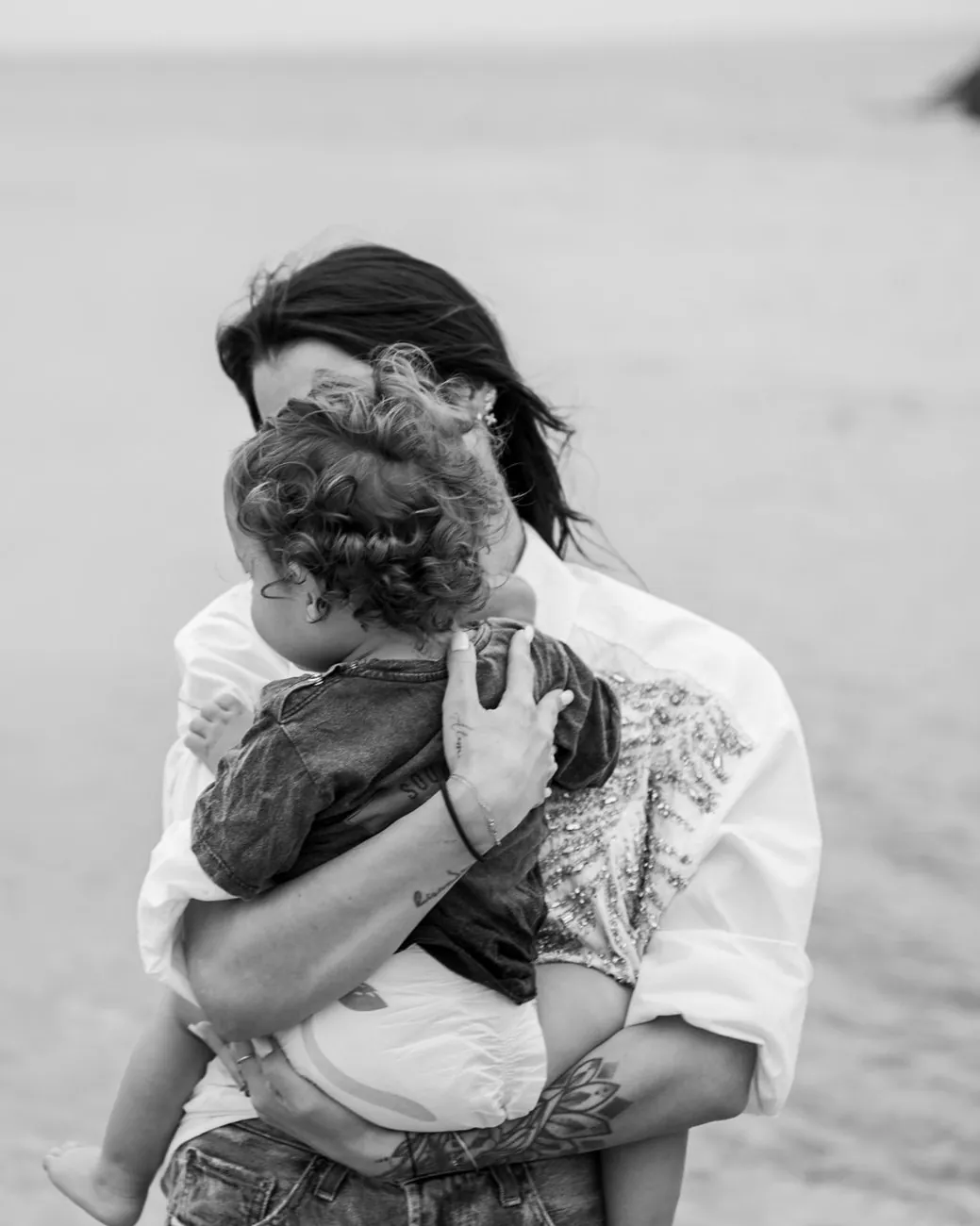 Family session by the water: a mum holding her curly-haired baby close, in black and white