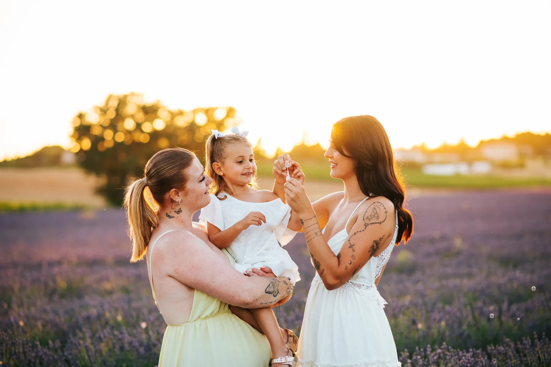 Family session in the lavender fields at sunset: two mums and their daughter blowing bubbles
