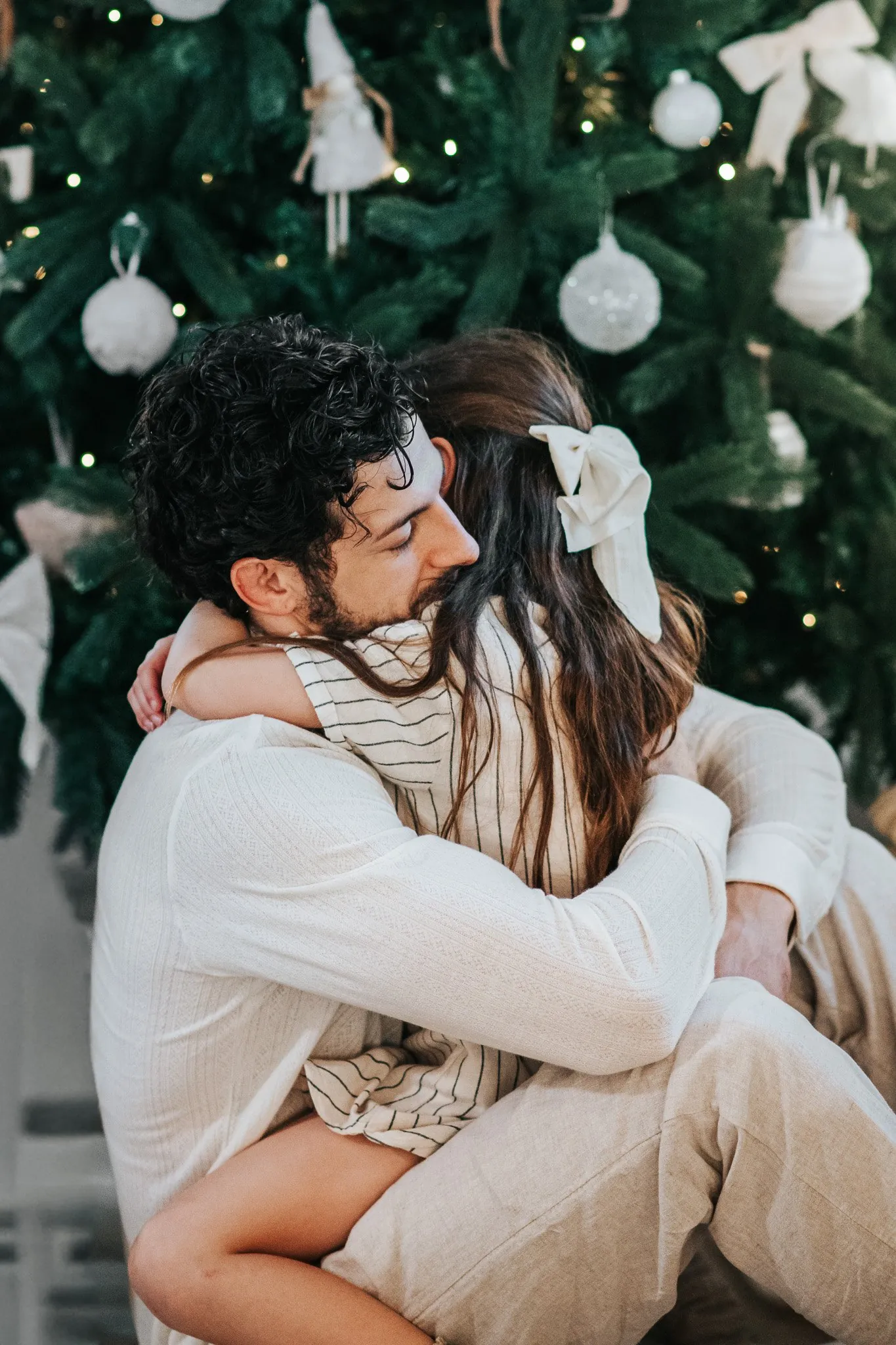 Christmas family session: a dad and his daughter in a long hug in front of a white-decorated tree