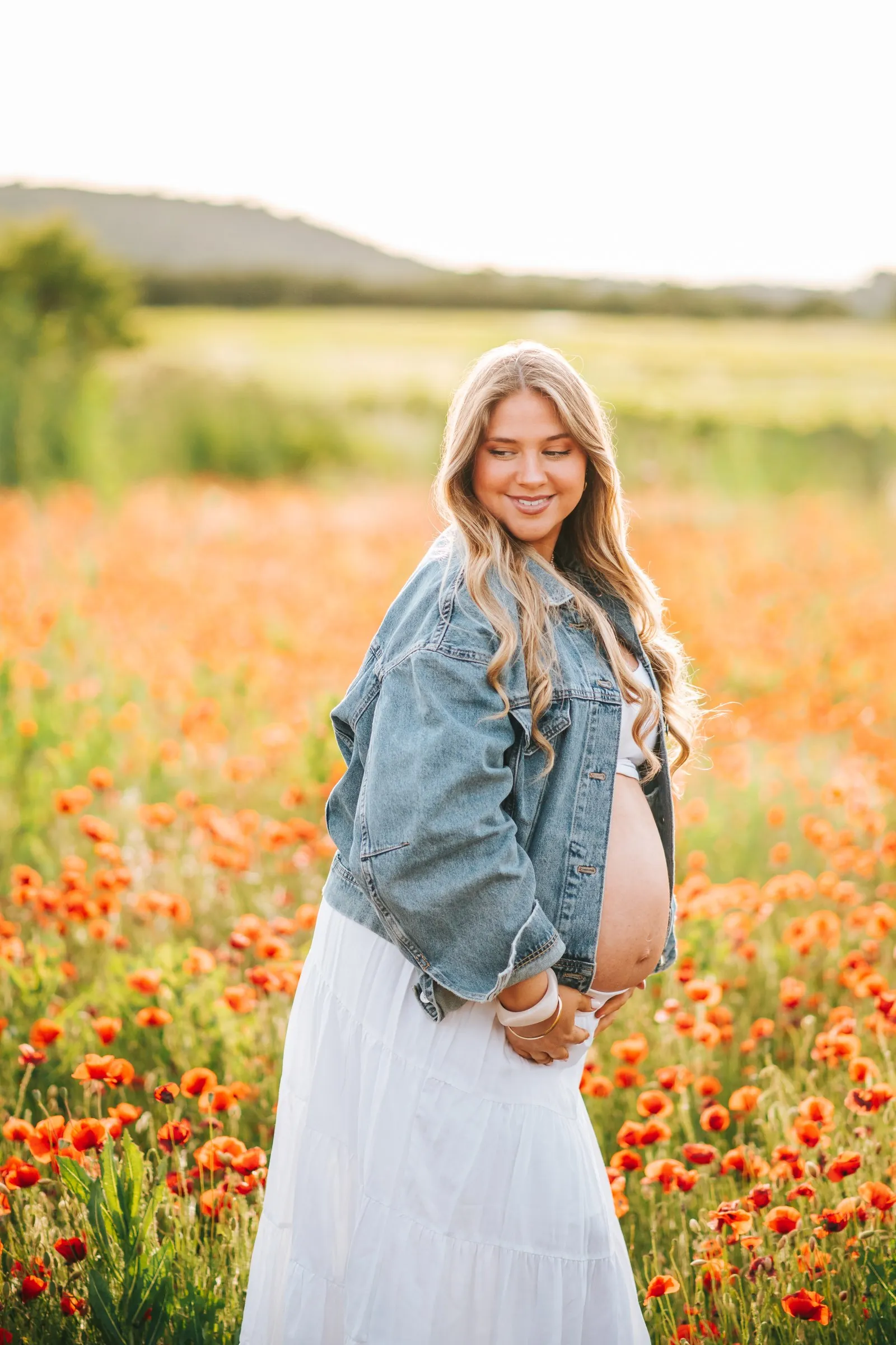 Séance grossesse dans les coquelicots en Provence : future maman souriante en veste en jean et jupe blanche