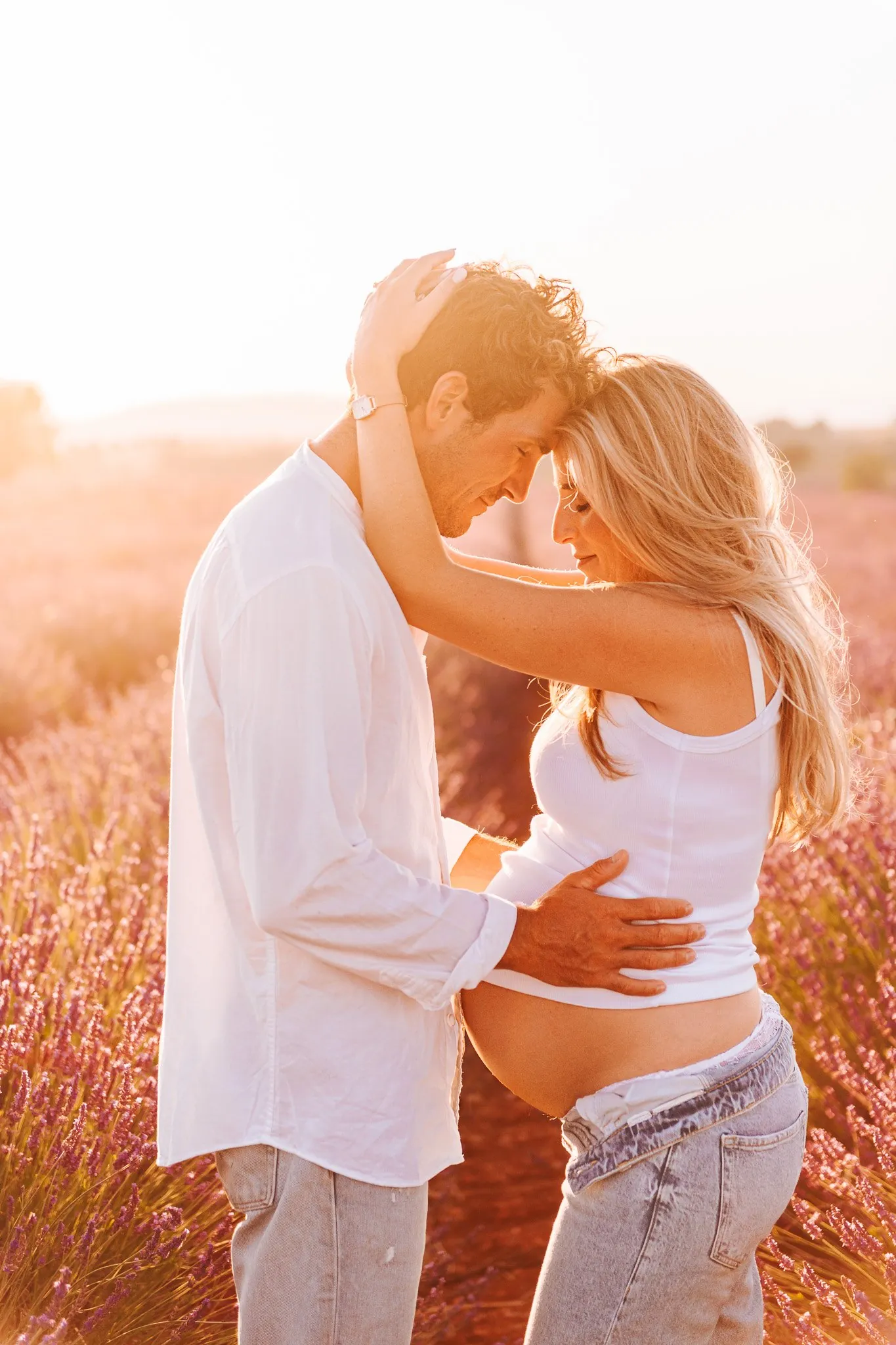 Maternity session in the lavender: a couple forehead to forehead, the dad-to-be's hand on the bump, golden light