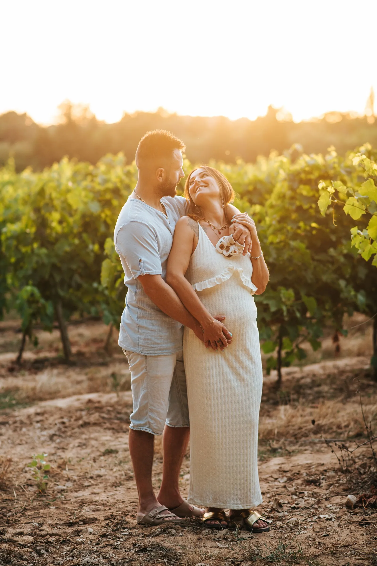 Séance grossesse dans les vignes au coucher du soleil, dans le Var : câlin du couple, mains sur le ventre