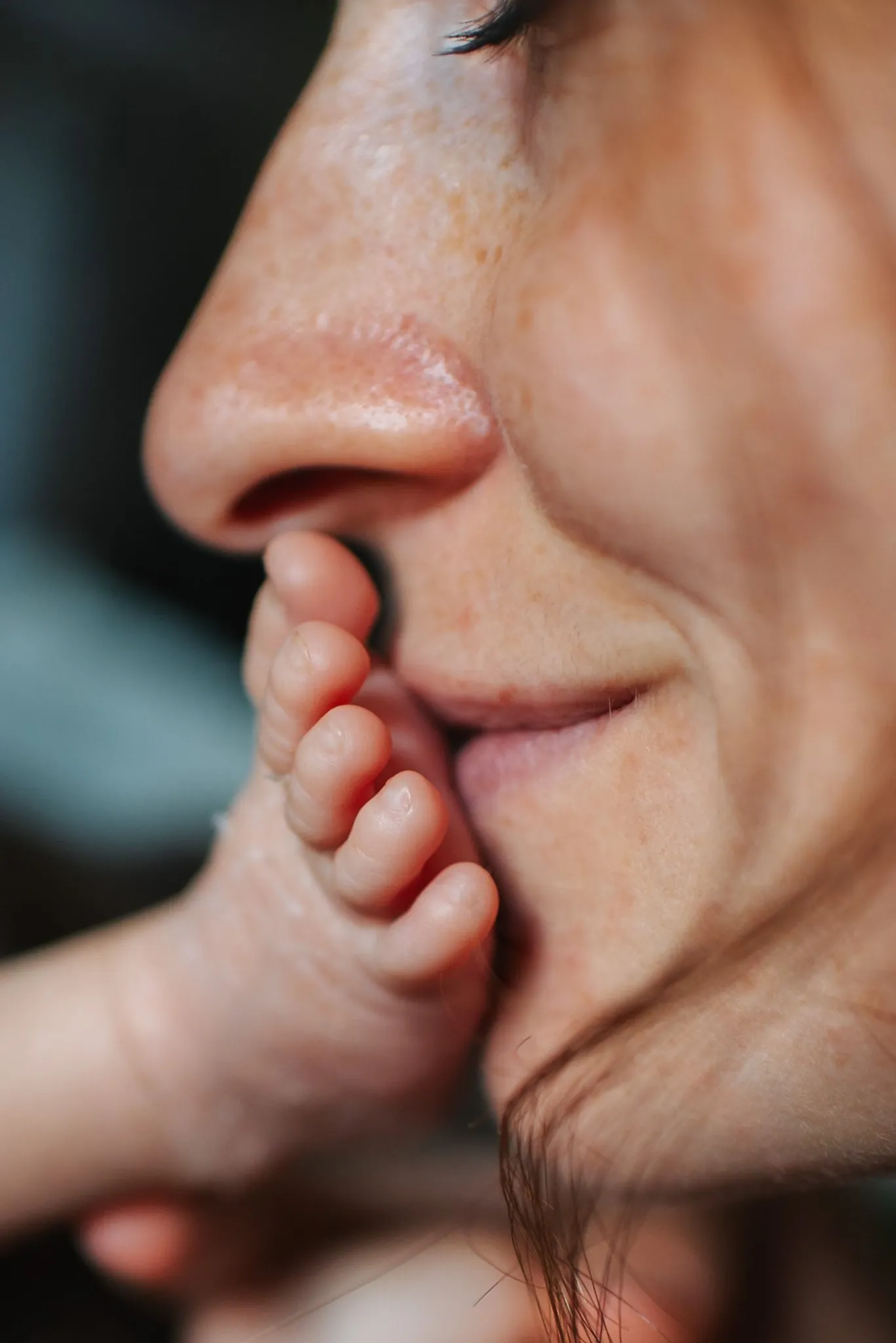 Séance naissance : maman souriante qui embrasse le petit pied de son bébé, gros plan plein de tendresse