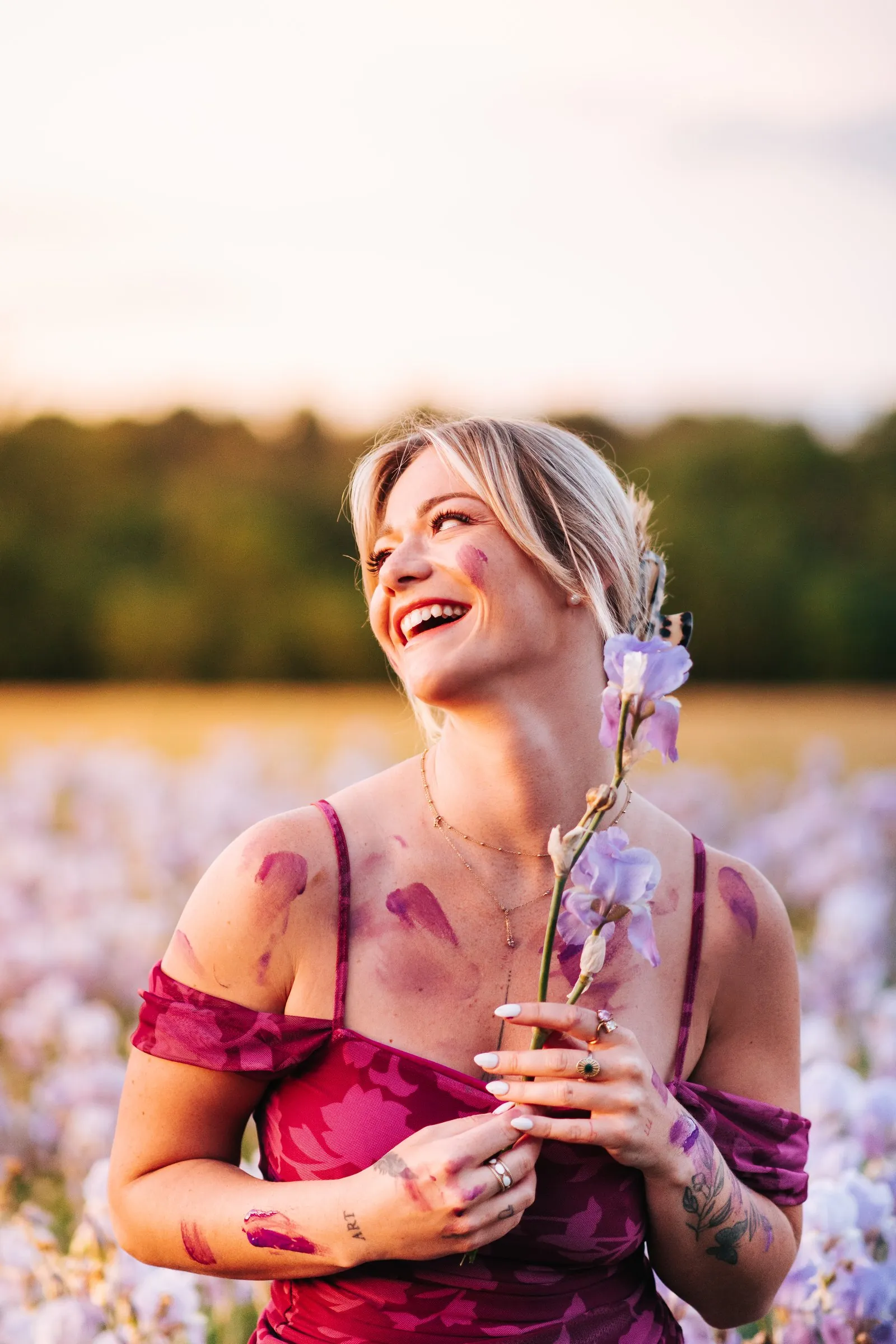 Portrait session in an iris field: a woman in a fuchsia dress laughing, holding a flowering stem, near Aix-en-Provence