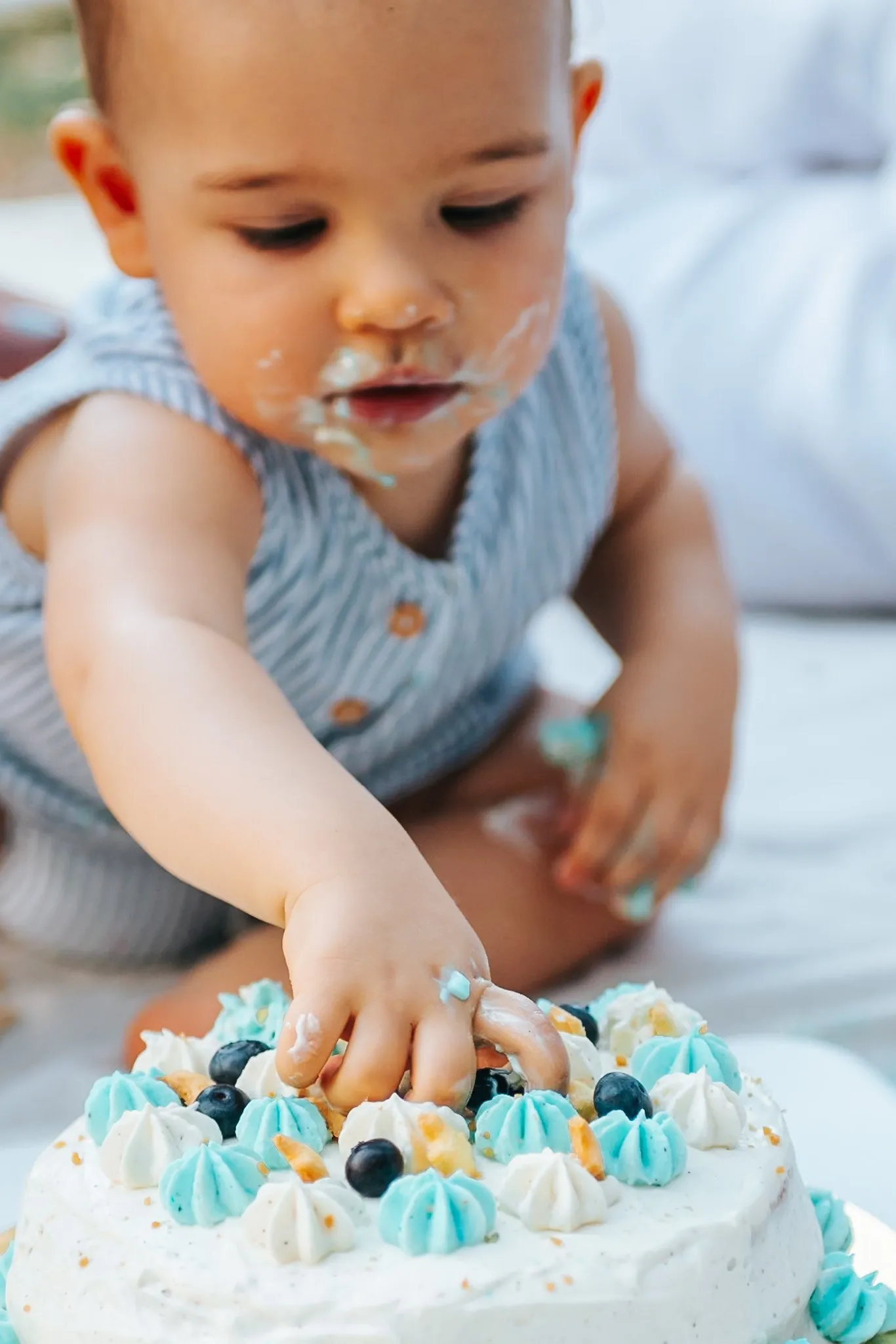 Smash cake des 1 an : petit garçon qui plonge la main dans un gâteau à la crème bleue, le visage barbouillé