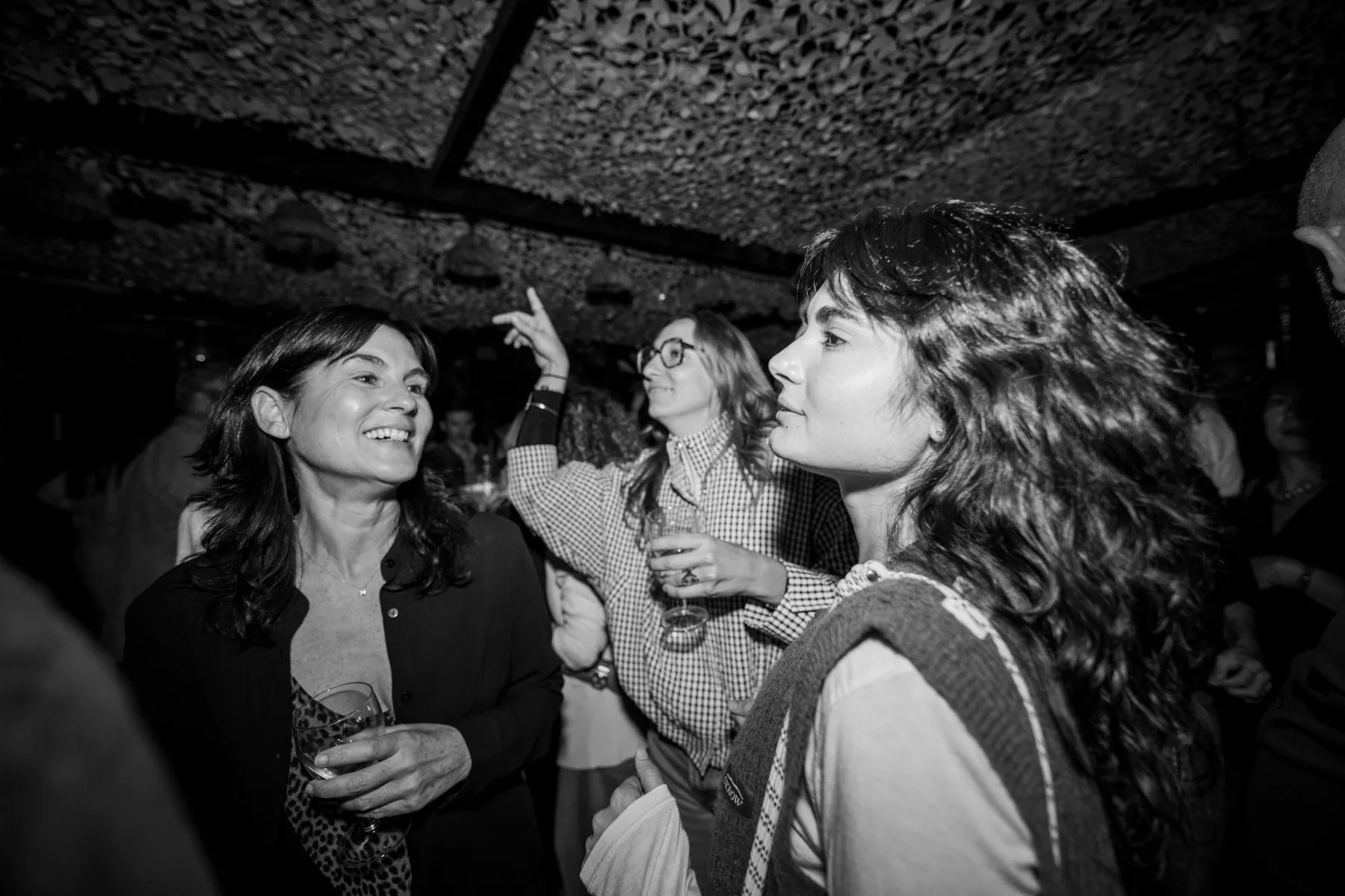 Soirée d'anniversaire : invitées qui dansent et rient, verre à la main, sous un plafond en filet, en noir et blanc