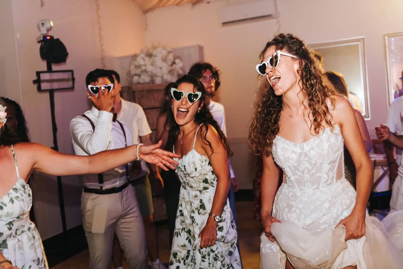 Soirée de mariage : la mariée et ses invités dansent en riant avec des lunettes en forme de cœur