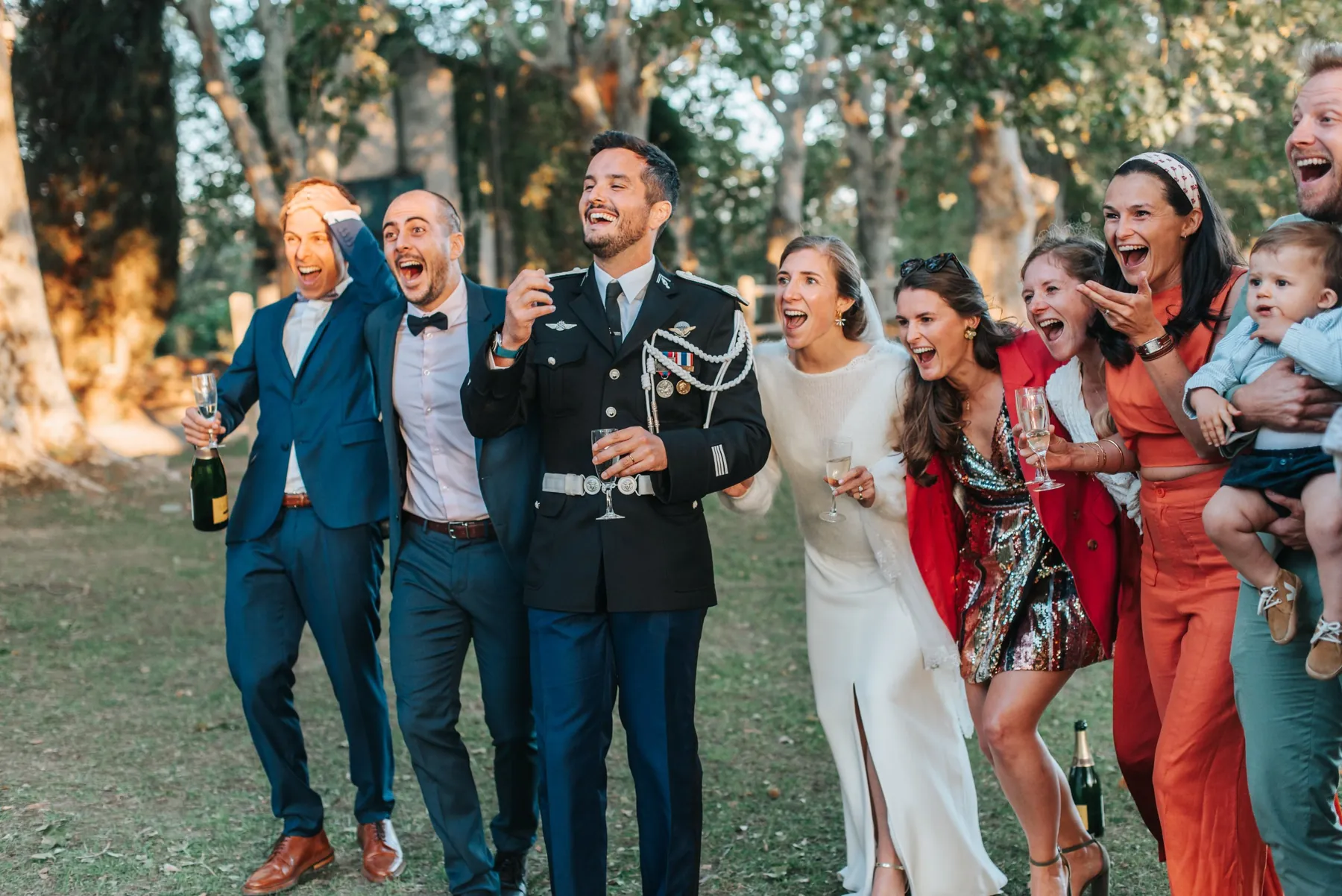 Mariés et invités, coupe de champagne à la main, qui crient de joie lors d'un vin d'honneur en plein air